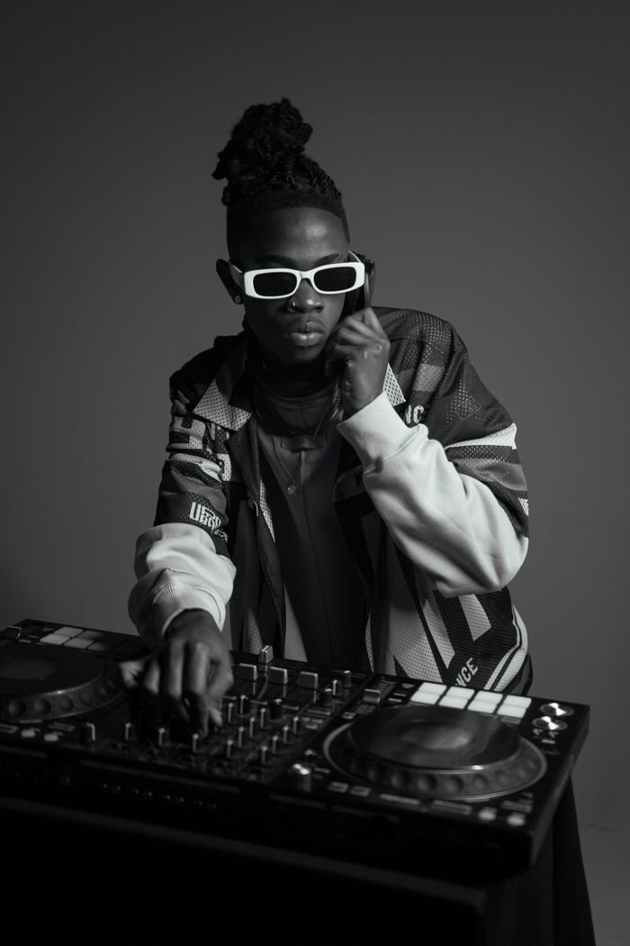 DJ with dreadlocks and sunglasses mixing music on a turntable in studio.